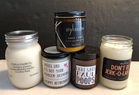 Lot of five scented soy candles in glass jars with lids, one missing a lid. Includes Citchcn Candle Co. Eucalyptus Spearmint, Stylissime Ambre + Chene, and three candles with humorous labels.