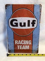 Full frontal image of the Gulf Racing Team tin sign showing design and condition with ruler for size reference.