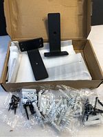 Six black metal wall shelf brackets and multiple packets of mounting hardware in original packaging.