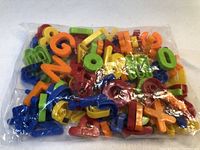 Clear plastic bag filled with colorful magnetic alphabet letters and numbers in various bright colors including red, orange, yellow, green, and blue.