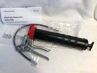 Photo of new heavy duty pistol grip grease gun with instruction manual on a light-colored surface.