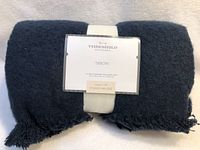 Folded navy blue throw blanket with label showing brand and design collaboration.
