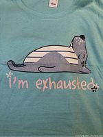 Close-up of light blue T-shirt with sleeping bear graphic and 'I'm exhausted' text