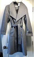 Front view of new women's long grey coat by Ricki's hanging on door, showing wide lapels, front pockets, and tie belt.