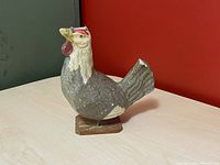 Side angle of wooden antique chicken toy showing red painted comb and wattles, wooden base and metal rod support.