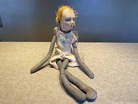 Front view of doll sitting, showing soft legs and arms with fabric construction and composite head with yellow hair.