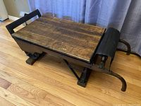 Left side view showing wooden plank top, cast iron wheel and curved tubular handle.