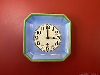 Front view of the vintage German ceramic plate clock face showing blue color with green border and black numbers and hands.