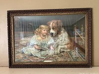 Framed lithograph print showing detailed scene of Victorian little girl reading a book to a Saint Bernard dog, in ornate wood frame under glass.