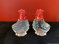 Front view of the two red chicken salt and pepper shakers with red tops and clear glass bodies.