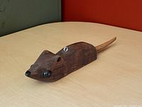 Angled front view of the hand-carved wooden mouse decoy with carved texture and dark brown finish on a light wood table.