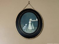 Full view of oval lithograph print of a girl and bulldog in black metal oval frame with gold accent and metal chain for hanging