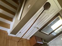 Full length view of the long wooden bread peel resting against a door, showing overall length and paddle shape.