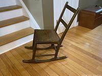 Side view of the antique child's rocking chair showing the plank seat, rockers, and ladder back design.