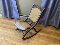 Full side view of the vintage cane folding rocking chair showing its wooden rockers, folding frame and cane seat and backrest.