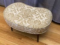 Vintage kidney bean foot stool hassock with beige and cream floral damask upholstery and tapered wooden peg legs.