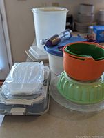 Overview showing a stack of containers including green jelly mold, orange container, clear cookie press, and other items wrapped in plastic.