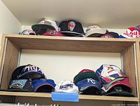 Shelving showing multiple baseball caps arranged in rows with various sports teams represented.