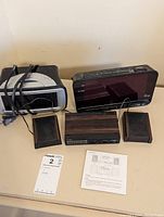 Full lot showing two digital clocks, tabletop radio with two speakers and instructions on beige table against beige wall.