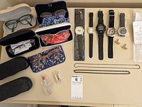 Overview of eyeglasses, watches, cases, repair kit, cufflinks and chains laid out on a surface