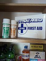 DynaMed Deluxe First Aid Kit box and two MED-FIRST first aid sprays on wooden shelf.