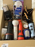 Photo showing multiple flashlights, clamps, and other handheld tools inside a cardboard box.