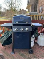 Full view of the black Dyna-Glo 3-burner gas propane grill with lid closed and two side shelves, positioned on a wooden deck.