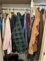 Wardrobe view of multiple jackets and coats hanging on rack showing color and styles: light pink quilted, green-black plaid, tan and brown coats