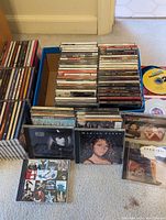 Wide shot showing several stacks of CDs in jewel cases, including placed-out albums by Mariah Carey, Bon Jovi, U2, and others.