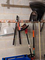 Tools hanging on wall including Fiskars Power Lever Lopper, Homelite trimmer, plastic and metal shovels, metal rake, and electrical cords.