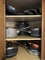 Overview of various pots and pans inside wooden cabinet shelves, showing different sizes and types, some with lids.