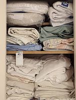 Closet shelves showing stacks of various folded bed linens and towels including a packaged InsulBloc item