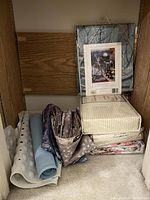 Shelf with folded sheet sets, rolled bathtub mats and floral fabrics.