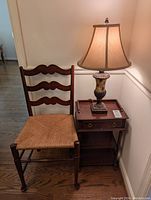 Photo of ladder back chair with woven seat and side table with urn style lamp on top.