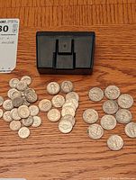 Top view of dispersed circulated U.S. nickels, dimes, and quarters with black plastic coin holder beside them on wooden surface.