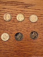 Top view of six U.S. vintage dimes laid on wooden surface showing different wear and designs