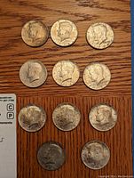 Top-down view of all 11 U.S. half dollar coins arranged in three rows, visible wear and tarnish, mostly dates from the 1960s with one 1980s coin among them.