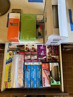 Photo showing multiple boxes of food storage bags, Glad Press'n Seal wrap, disposable plastic wrap, and part of the straws box and green napkins.