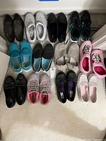 Photo showing a set of 14 pairs of women's footwear in various colors and styles, arranged in three rows on the floor.