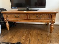 Front view of wood coffee table with two drawers and turned legs on hardwood floor, showing wear and blemishes.