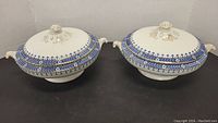 Two closed vintage casserole dishes with lids showing blue and gold decorative trim and handles.