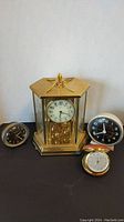 Four clocks on black surface: Large Kundo carriage clock in center with three smaller Westclox clocks around it.