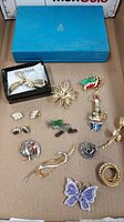 Grouped photo of costume brooches and earrings including items in Braemar boxes placed on a cardboard surface.