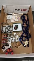 Box containing a variety of costume jewelry pieces including necklaces, bracelets, earrings, and pins displayed together
