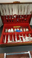 Open wooden chest displaying the flatware pieces organized in rows on red velvet lining.