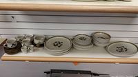 Overview of all pieces arranged on shelf showing cups, saucers, plates and bowls