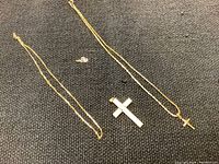 Overview of two gold necklaces and a large cross pendant on black cloth