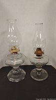 Two clear glass kerosene oil lamps, one with hexagonal base and one with round base, brass burners and glass chimneys