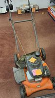 Front perspective of the orange and black gas lawn mower with visible handlebar and engine.