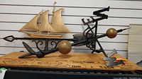 Photo showing full weather vane with black metal base, gold ship detail, cardinal direction markers, and spherical accents on horizontal bar.